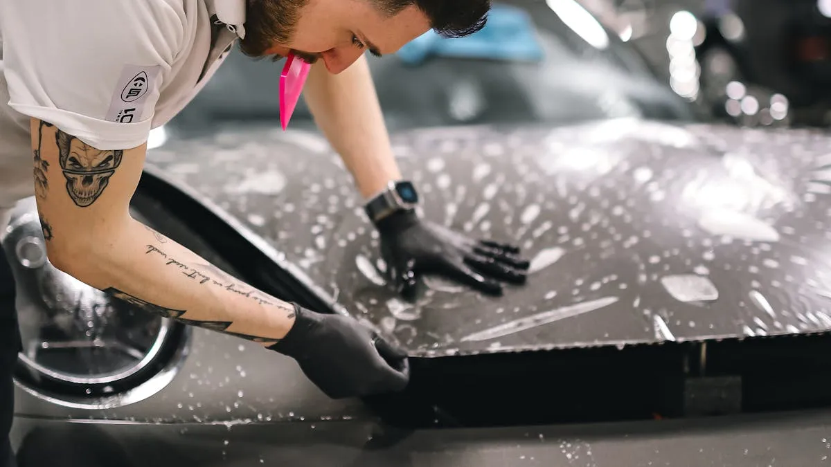 Hand washing a dark sedan with a microfiber mitt on a shaded driveway